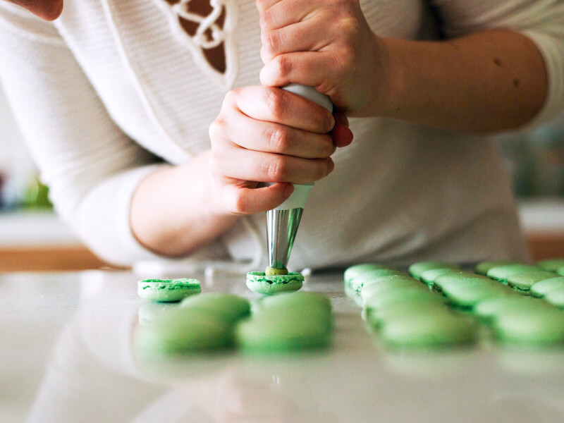 A person is piping rows of green macarons